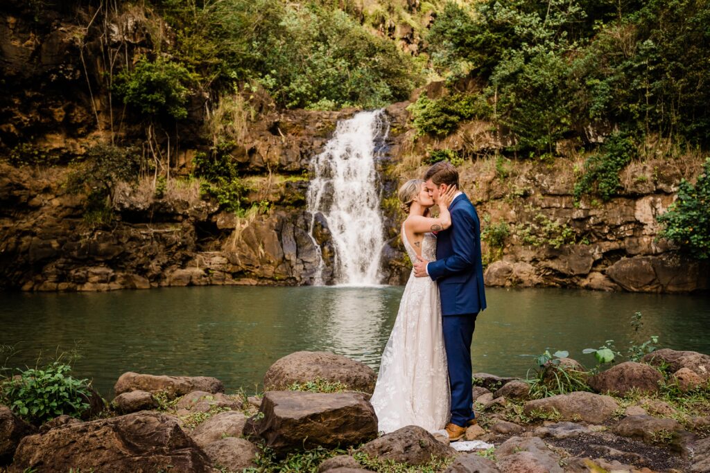 Couple kisses under water fall after getting married at Waimea Valley, Oahu