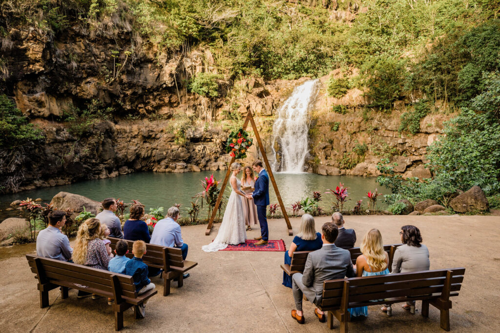 Couple gathers under a waterfall for small wedding ceremony in Hawaii at Waimea Valley, Oahu. 