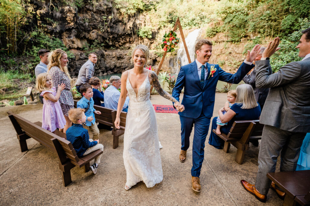 Couple smiles and high-fives their family members after getting married at Waimea Valley in Oahu. 
