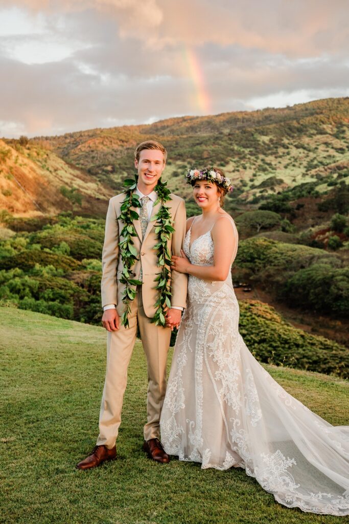 A couple poses for a picture at the foothills of a lush and green mountain on the North Shore of Oahu, Hawaii.