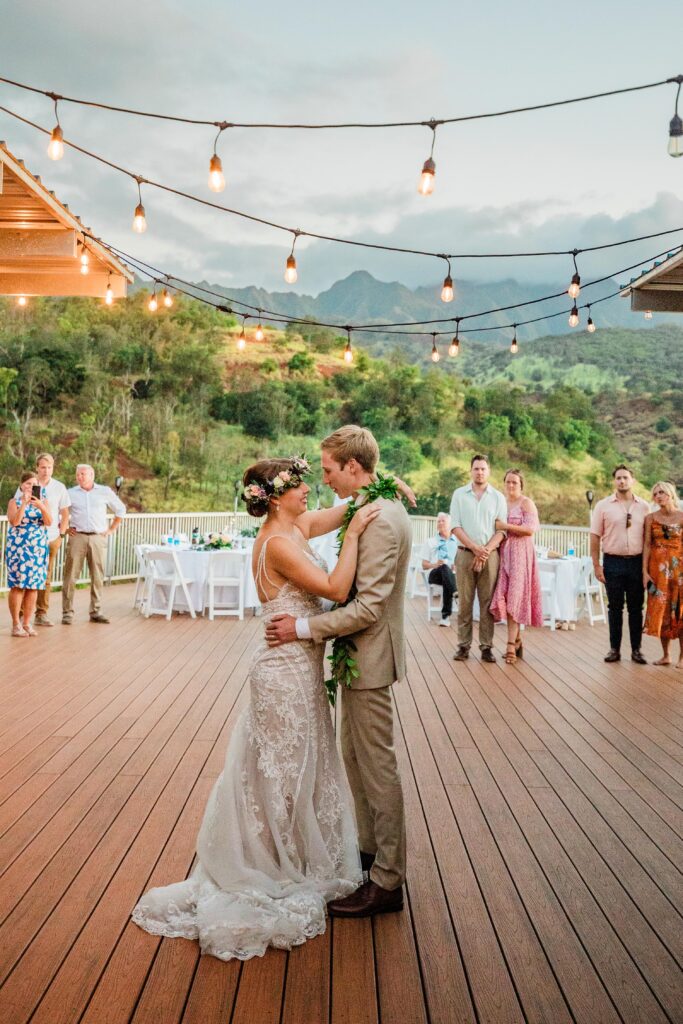 Newly married couple has their first dance on a large deck with a gorgeous green mountain background