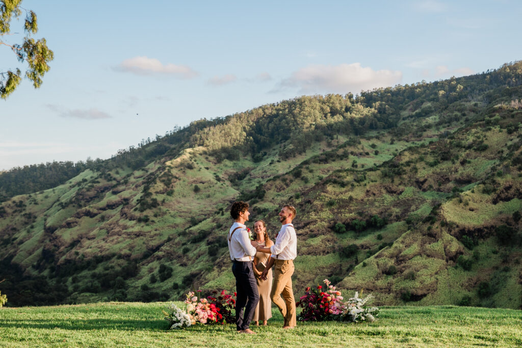 A gay couple happily rejoices during their wedding ceremony at a venue in the mountains of Oahu, Hawaii.